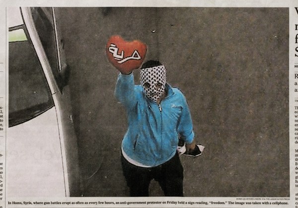 “In Homs, Syria, where gun battles erupt as often as every few hours, an anti-government protester on Friday held a sign reading ‘freedom’. The image was taken with a cellphone.” The photo is credited to “Homs Quarters Union, via The Associated Press”.